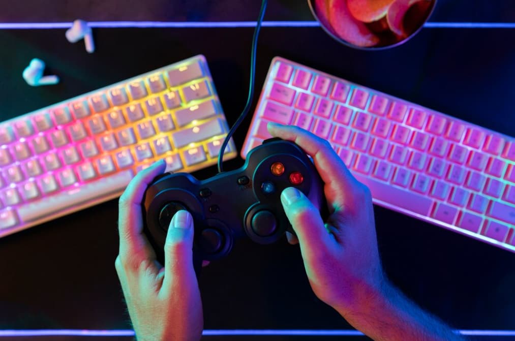 Hands gaming with a controller, keyboard, and colorful backlighting