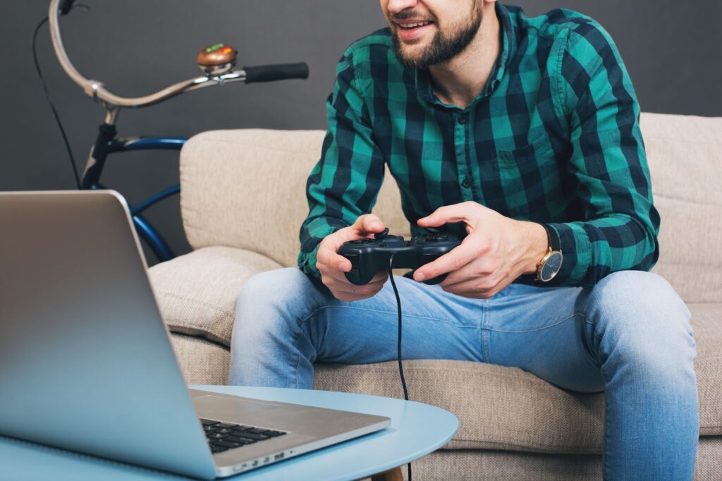Man sitting on couch at home and playing video game on notebook